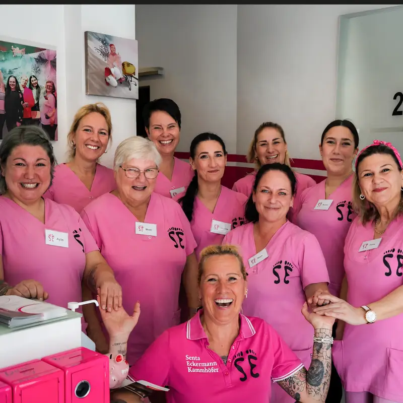 Gruppe lachender Personen in pinker Kleidung mit Namensschildern und Fotos